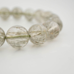 A luxury flexible natural stone bracelet made of 11-12mm round smooth clear quartz beads with sharp green rutilated inclusions.