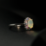 A luxury designer jewelry set including a ring, earrings, and necklace made of original oval cabochon opals surrounded by a multicolor sapphire halo in 925 sterling silver.
