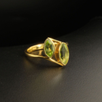A gold-plated 925 sterling silver women's ring featuring two natural marquise-shaped faceted green peridot gemstones in a bezel setting.