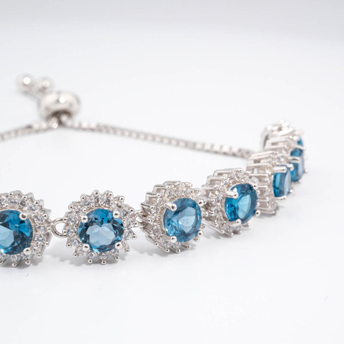 Bracelet coulissant de haute joaillerie en argent 925 avec topazes London blue naturelles et halo de zircons étincelants.