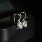 A luxurious pair of 925 sterling silver dangle hook earrings featuring oval faceted natural blue topaz gemstones.