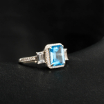 An authentic natural faceted emerald-cut Swiss blue topaz gemstone 925 silver halo ring with baguette side stones.