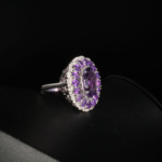 Bague de prestige en argent 925 ornée d'une améthyste naturelle taille ovale entourée d'un double halo de pierres étincelantes sur fond noir.