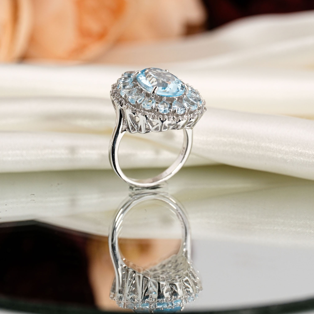 Bague de prestige en argent 925 ornée d'une topaze bleue naturelle taille ovale entourée d'un double halo de pierres étincelantes sur fond noir.
