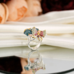 Bague artistique pour femme en argent 925 avec fleur sculptée en aigue-marine et papillon en tourmaline rose sur velours rouge.