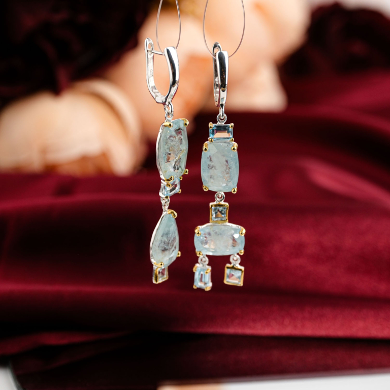 Boucles d'oreilles pendantes d'exception en argent 925 ornées d'aigue-marine naturelle et topaze bleue sur fond rouge bordeaux.