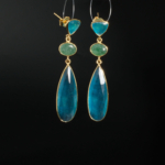 Boucles d'oreilles pendantes d'exception en argent 925 plaqué or ornées de quartz bleu et d'émeraude naturelle sur fond noir.