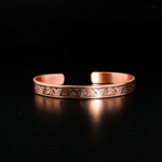 Bracelet jonc ouvert artisanal en cuivre pur avec gravures florales traditionnelles sur satin blanc.