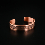 Bracelet jonc ouvert artisanal en cuivre pur avec gravures de protection traditionnelles sur satin blanc.