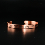 Bracelet jonc ouvert artisanal en cuivre pur avec gravures géométriques traditionnelles sur satin blanc.