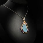 Collier artistique pour femme avec aigue-marine sculptée en fleur et tourmalines roses en argent 925 sur satin blanc.