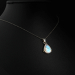 Pendentif goutte raffiné pour femme en pierre de lune naturelle à reflets bleus et chaîne argent 925 sur fond sombre.
