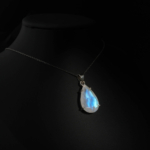 Collier fin pour femme avec pendentif goutte en pierre de lune naturelle facettée à éclat bleu sur satin vert émeraude.