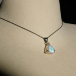 Damen Anhänger Kette aus 925 Silber mit facettiertem blau schimmerndem Tropfen Mondstein auf dunklem Hintergrund.