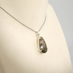 Damen Anhänger Kette aus 925 Silber mit facettiertem Tropfen Rutilquarz mit schwarzen Nadeln auf weißer Seide.