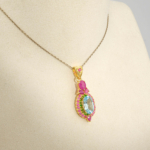 Damen Anhänger Kette aus 925 Silber vergoldet mit facettiertem blauem Topas, Tsavorit und Rubin-Kranz auf weißer Seide.