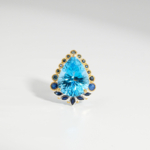 Damen Ring aus 925 Silber mit blauem Topas im Tropfenschliff und Saphir Halo auf weißer Seide.
