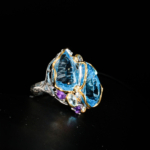 Genuine natural sky blue topaz double pear cut faceted stones with amethyst accents two tone 925 sterling silver statement ring black background.