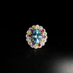 Natural oval blue topaz cocktail ring with citrine, amethyst, garnet, and peridot halo in 925 sterling silver on white satin.