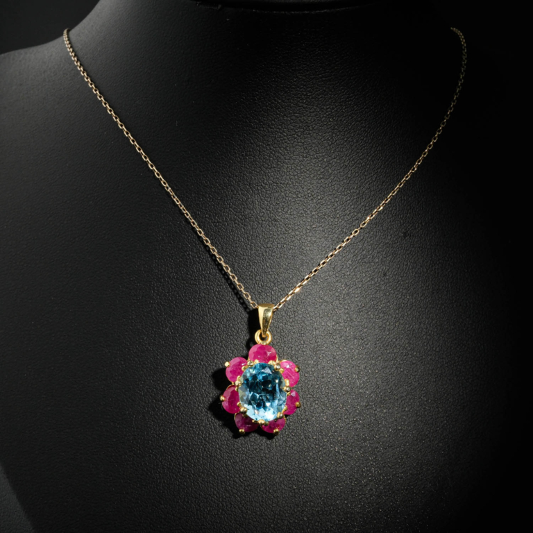 Natural faceted oval blue topaz pendant necklace with ruby flower halo in gold plated 925 silver on white satin.