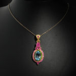 Natural faceted oval blue topaz pendant necklace with green tsavorite and ruby halo in gold plated 925 silver on white satin.