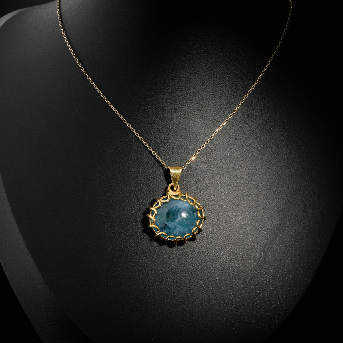 Natural oval cabochon deep blue aquamarine gemstone pendant necklace with braided gold plated 925 silver setting on white satin.