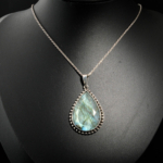 Natural faceted teardrop blue green flash labradorite gemstone pendant necklace in 925 sterling silver on white satin.