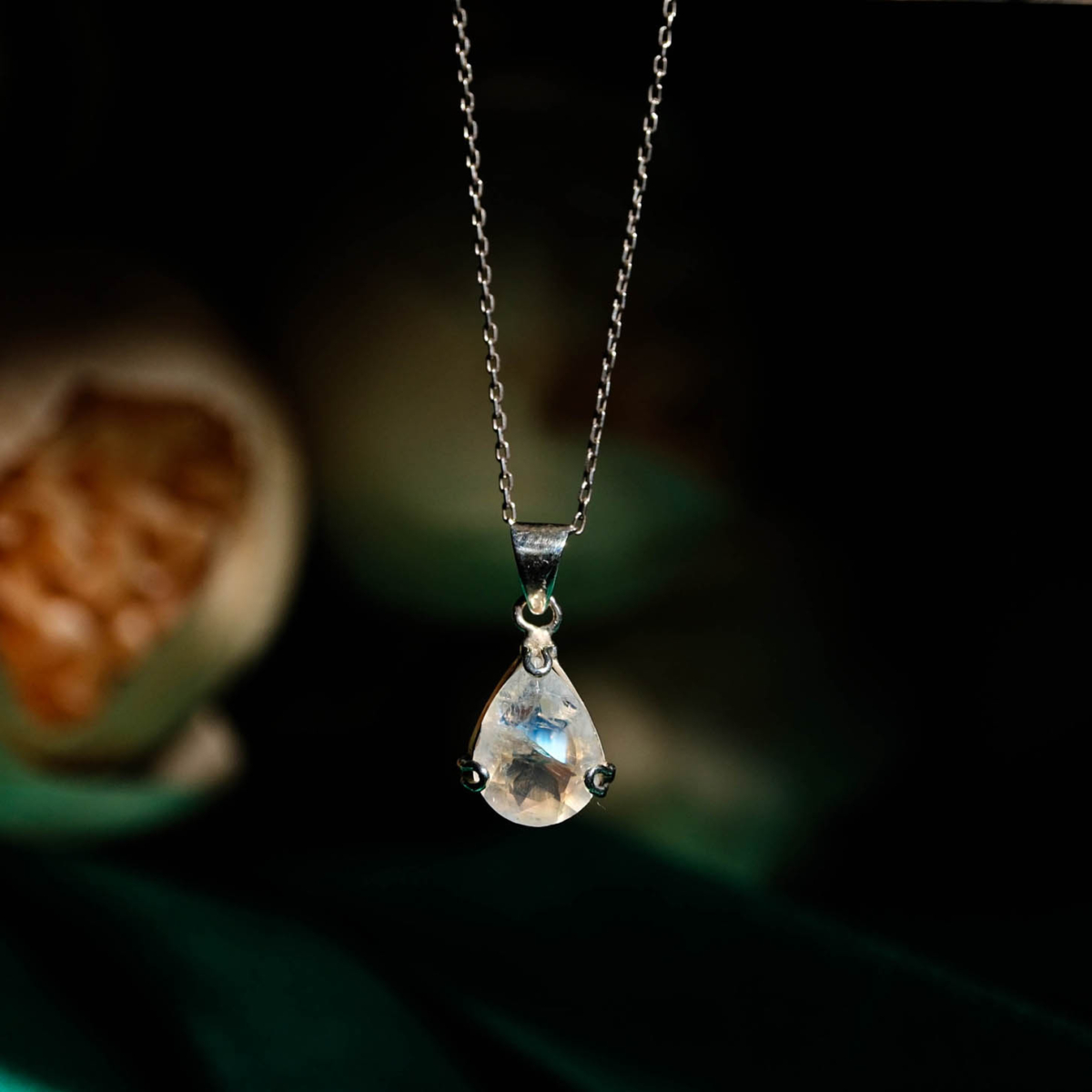 Natural faceted teardrop blue flash moonstone gemstone pendant necklace in 925 sterling silver on dark backdrop
