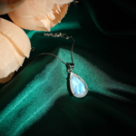Natural faceted teardrop blue flash moonstone gemstone pendant necklace in 925 sterling silver on emerald green satin.