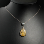 Natural faceted teardrop golden rutilated quartz gemstone pendant necklace in 925 sterling silver on white satin