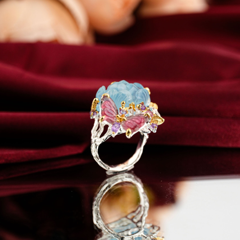 Hand carved blue aquamarine peony flower and pink tourmaline butterfly statement ring in 925 sterling silver on red velvet.