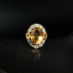 Natural faceted oval yellow citrine statement ring with blue topaz halo in two-tone 925 silver on white satin.