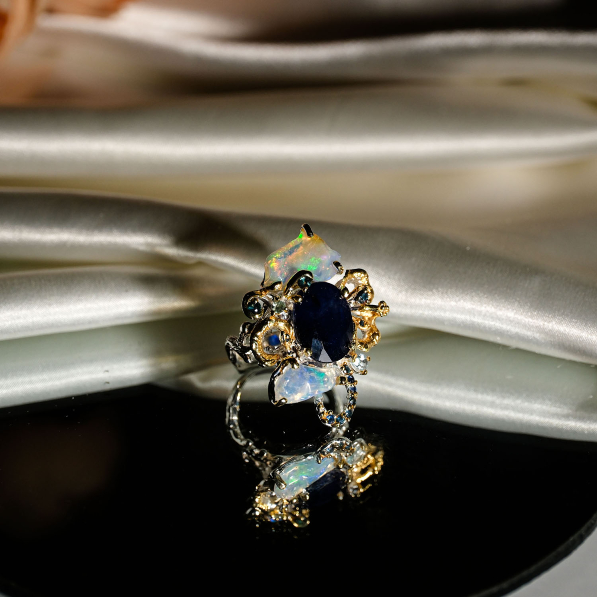 Natural faceted oval blue sapphire statement ring with opal slices and topaz in two-tone 925 sterling silver on white satin.