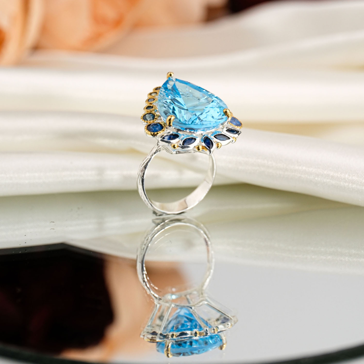 Natural faceted pear cut blue topaz ring with sapphire halo in 925 sterling silver on white satin.