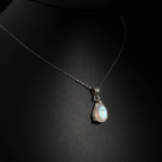 Natural faceted teardrop rainbow moonstone gemstone pendant necklace in 925 sterling silver on dark background.