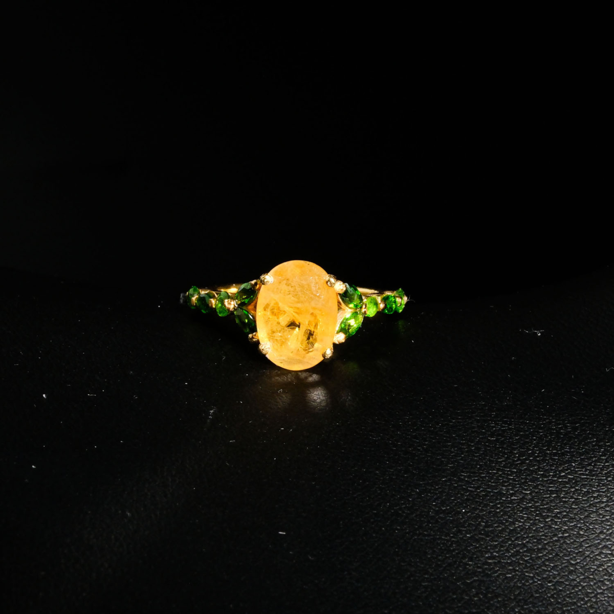 Genuine natural yellow sapphire oval gemstone surrounded by green tsavorite garnet halo yellow gold plated 925 sterling silver statement ring black background.