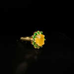 Genuine natural yellow sapphire oval gemstone surrounded by green tsavorite garnet halo yellow gold plated 925 sterling silver statement ring black background.