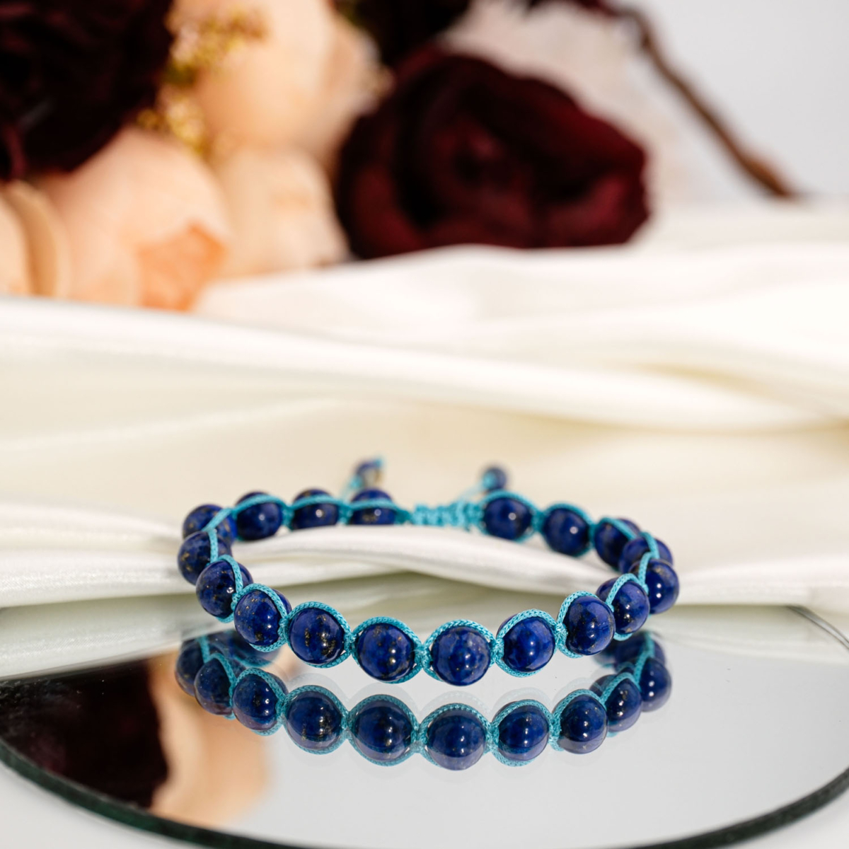 Beyaz saten kumaş ve ayna üzerinde altın pirit pırıltılı 5A kalite 8 mm küre lapis lazuli taşlı turkuaz makrome örme bileklik.