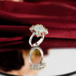 Beyaz saten kumaş ve ayna üzerinde pastel mavi akuamarin etrafında kırmızı baget garnet taşlı altın tırnaklı 925 ayar gümüş kadın yüzük.