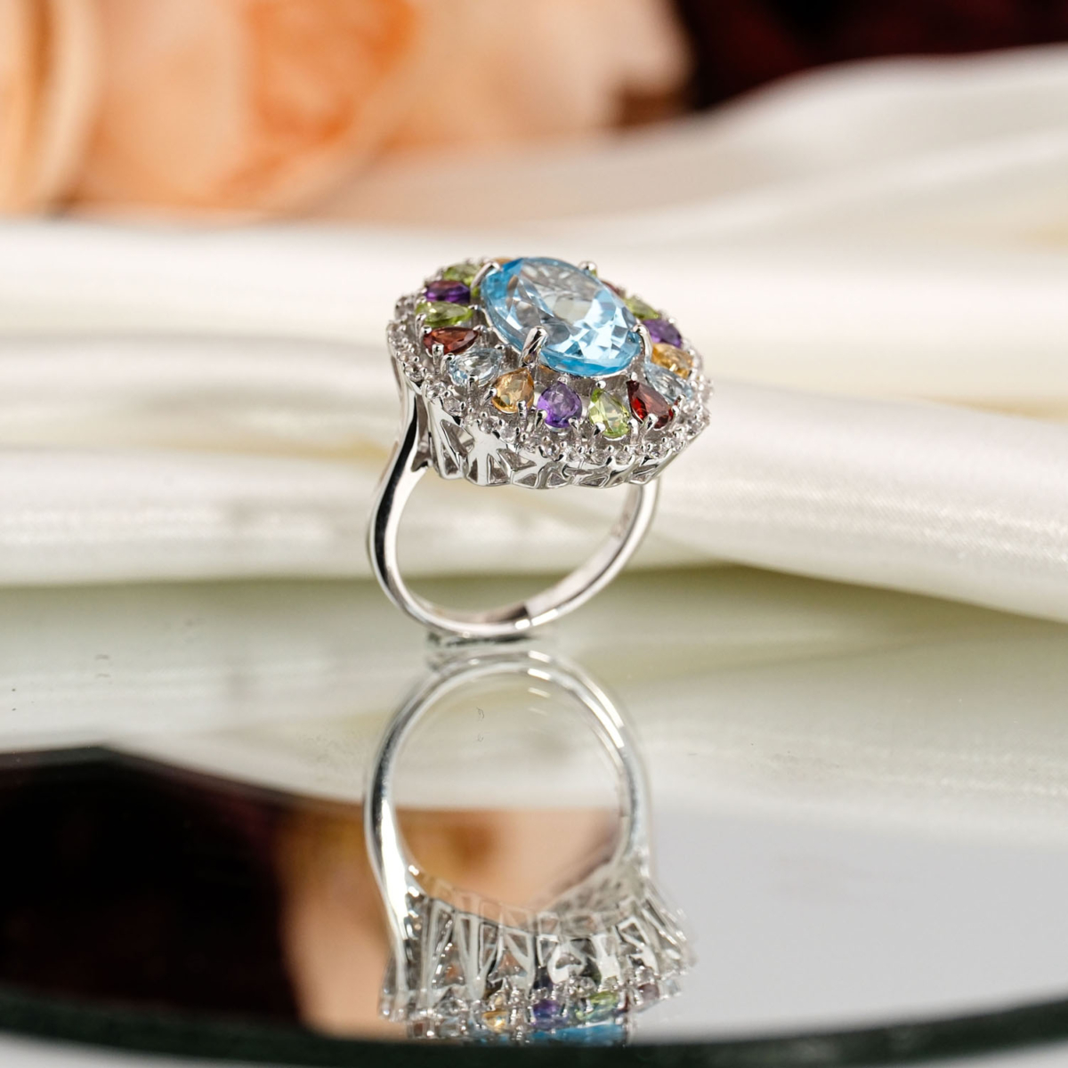 Beyaz saten kumaş ve ayna üzerinde faset oval açık mavi topaz etrafında sitrin, ametist, garnet ve zebercet taşlı saray tasarım 925 gümüş kadın yüzük.