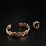 Parure artisanale en cuivre pur tressé avec bracelet jonc ouvert et bague ajustable sur satin blanc.