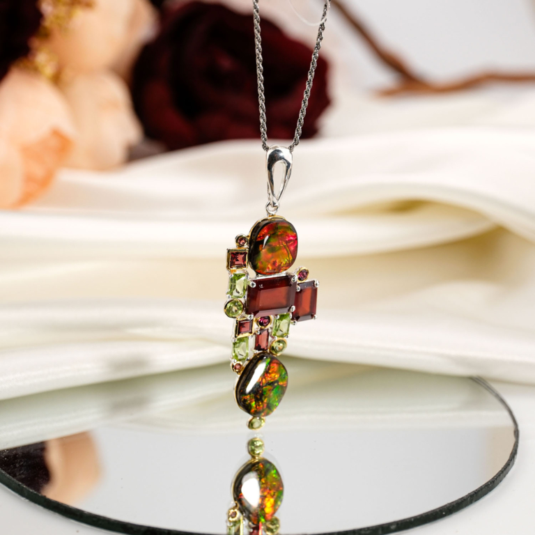 Pendentif de prestige en argent 925 orné d'ammolite opale naturelle, grenat rouge, rubellite et péridot sur présentoir en bois.
