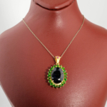 Damen Anhänger Kette aus 925 Silber vergoldet mit ovalem blauem Saphir und grünem Tsavorit Kranz auf weißer Seide.